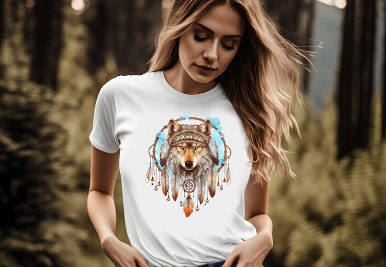 Pode incluir: Camiseta branca com um lobo castanho usando uma coroa dentro de um apanhador de sonhos azul e castanho com penas.