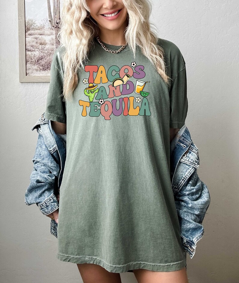 Puede incluir: Una camiseta verde con un gr&aacute;fico de estilo retro que dice "Tacos and Tequila" con ilustraciones de tacos, un cactus, un sombrero y una copa de margarita.