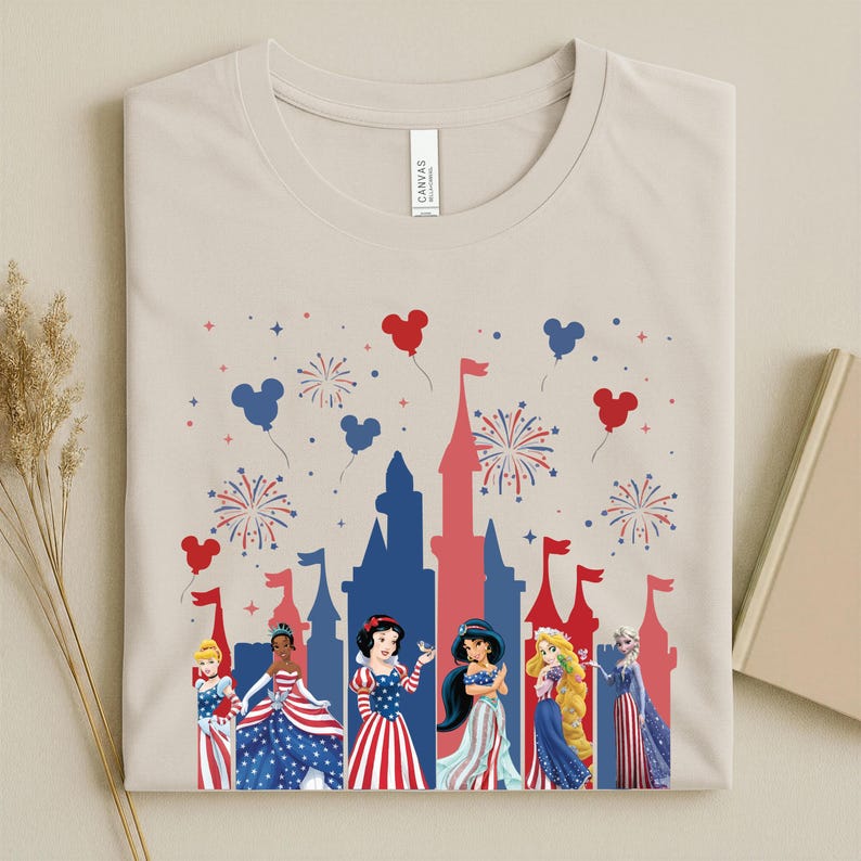 May include: Beige t-shirt with a patriotic design, featuring a red and blue castle silhouette, fireworks, and Mickey Mouse balloons. The shirt displays Disney princesses in red, white, and blue dresses. The word "CANVAS" is printed on the shirt.