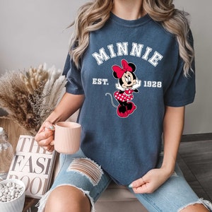 May include: A navy blue t-shirt with a white graphic of Minnie Mouse and the text "Minnie Est. 1928".
