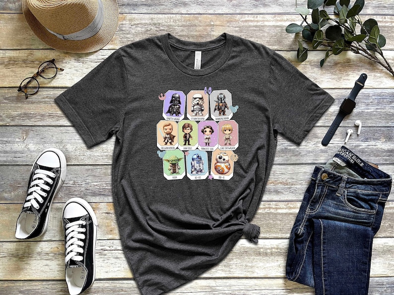 May include: A dark heather grey t-shirt with a graphic print of various Star Wars characters in a grid pattern. The characters are depicted in a chibi style, with large heads and small bodies. The characters include Darth Vader, Stormtrooper, Boba Fett, Luke Skywalker, Han Solo, Princess Leia, Yoda, R2-D2, and BB-8.