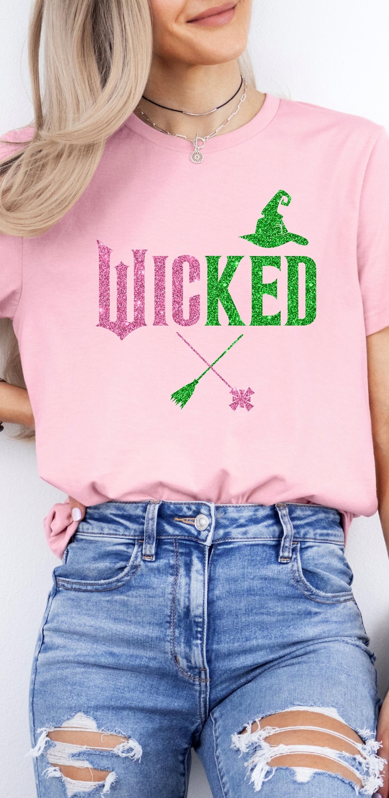 May include: Pink t-shirt with the word "WICKED" in glittery pink and green. A green witch hat, a broom, and a star-shaped design are also featured. The shirt is paired with blue jeans.
