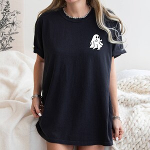 May include: A black oversized t-shirt with a white ghost graphic on the front. The ghost is wearing a smile and has two arms outstretched.