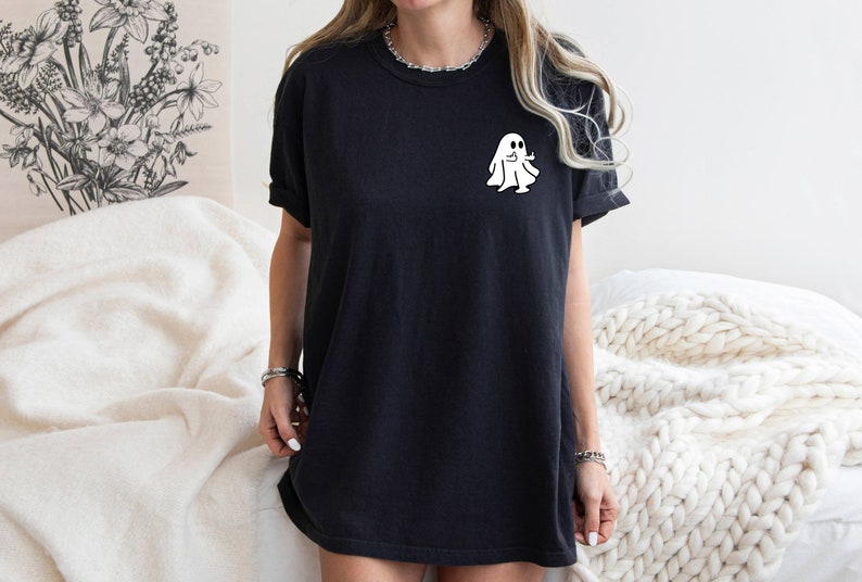 May include: A black oversized t-shirt with a white ghost graphic on the front. The ghost is wearing a smile and has two arms outstretched.