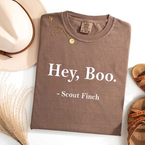 May include: A brown t-shirt with the text "Hey, Boo. - Scout Finch" printed in white.