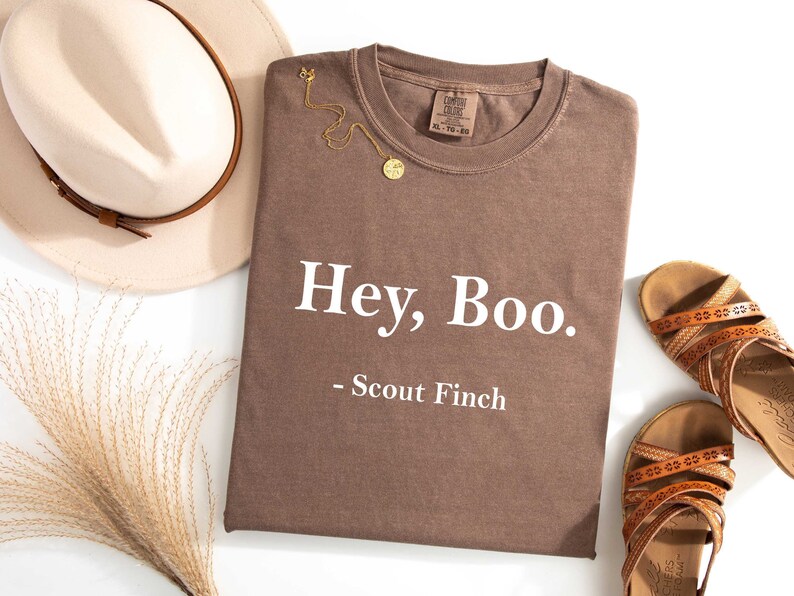 May include: A brown t-shirt with the text "Hey, Boo. - Scout Finch" printed in white.
