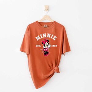May include: A rust-colored t-shirt with a white graphic of Minnie Mouse and the text "Minnie Est. 1928".