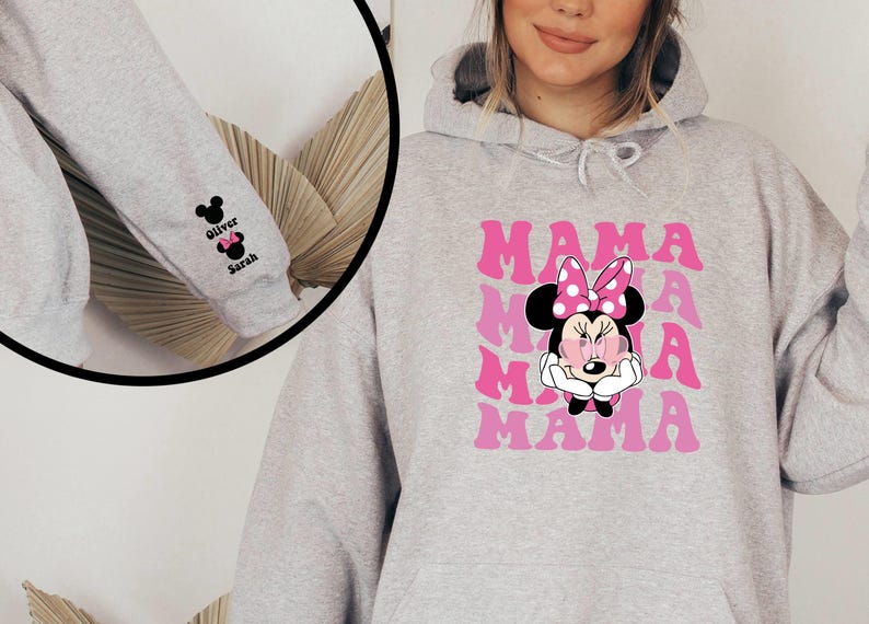 Puede incluir: Sudadera gris con un gr&aacute;fico rosa y blanco de Minnie Mouse y la palabra "MAMA" repetida. La manga tiene un gr&aacute;fico en blanco y negro de Minnie Mouse con los nombres "Oliver" y "Sarah" debajo.