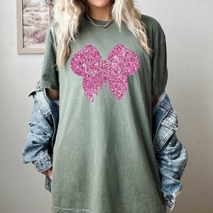 May include: A green oversized t-shirt with a pink glitter bow design.
