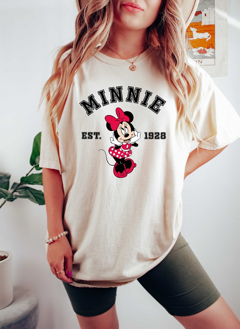 May include: A white t-shirt with a black and white graphic of Minnie Mouse. The graphic includes the text "MINNIE EST. 1928".
