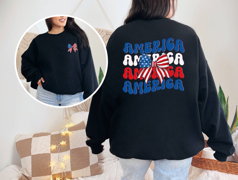 K&ouml;nnte beinhalten: Schwarzer Pullover mit einer rot-wei&szlig;-blauen Schleife und dem Wort "AMERICA", das viermal in einer Retro-Schrift wiederholt wird.