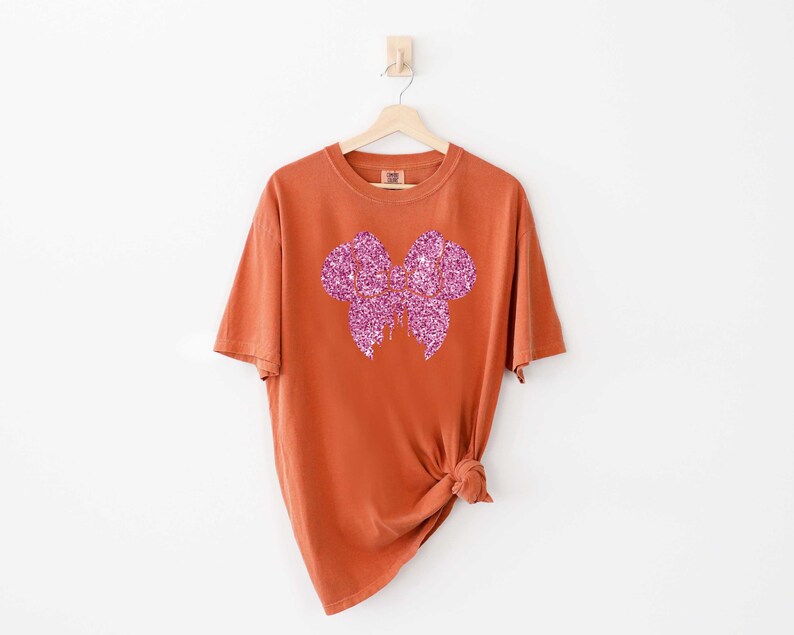 May include: A rust-colored t-shirt with a pink glitter bow design.