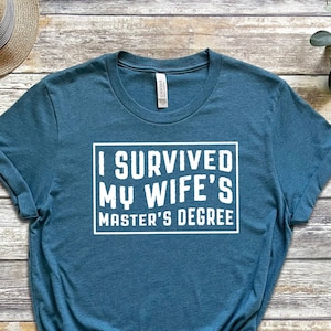 May include: A teal blue t-shirt with white text that reads "I survived my wife's master's degree".