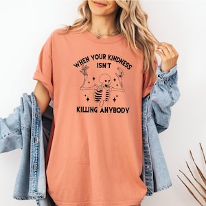 May include: A peach-colored t-shirt with a black skeleton graphic and the text "When your kindness isn't killing anybody".