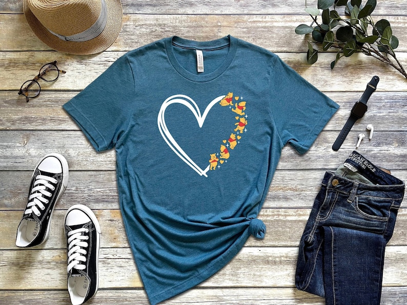 May include: A teal blue t-shirt with a white outline of a heart and a line of Winnie the Pooh bears in yellow and red inside the heart.