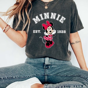 May include: A charcoal gray t-shirt with a vintage-style graphic of Minnie Mouse. The graphic includes the text "Minnie Est. 1928".