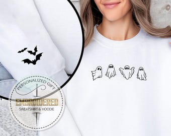 May include: White sweatshirt with black embroidered Halloween-themed designs. The sleeve features three bat silhouettes. The front displays four ghost figures. The design is part of an embroidered sweatshirt and hoodie collection.