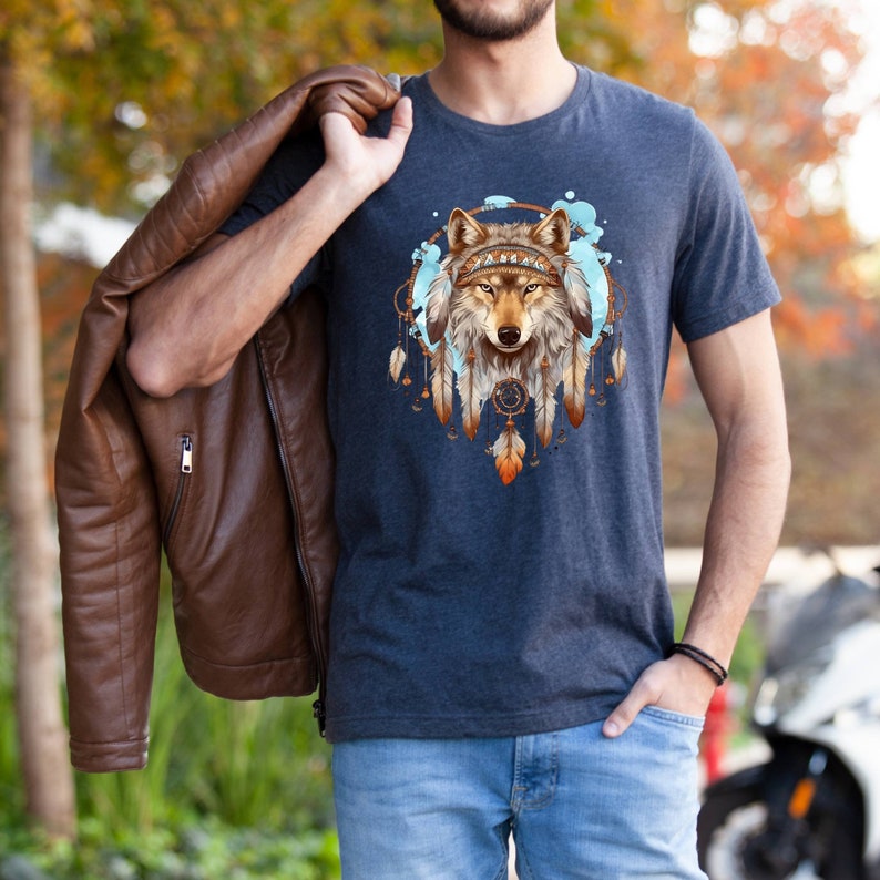 Pode incluir: Uma camiseta azul marinho com um gr&aacute;fico de uma cabe&ccedil;a de lobo dentro de um apanhador de sonhos com penas. O apanhador de sonhos &eacute; rodeado por respingos de aquarela azul e branca.