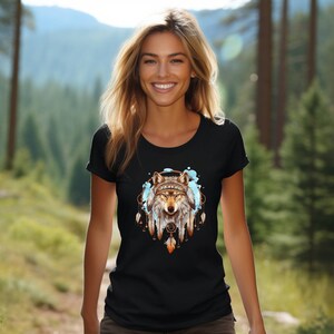 Pode incluir: Camiseta preta com a cabe&ccedil;a de um lobo dentro de um apanhador de sonhos com penas. O lobo est&aacute; usando uma faixa de contas. O apanhador de sonhos &eacute; cercado por respingos azuis como aquarela.