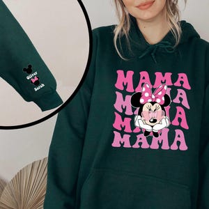 Puede incluir: Una sudadera con capucha verde oscuro con un gr&aacute;fico rosa y blanco de Minnie Mouse y la palabra "MAMA" repetida. La sudadera tiene una capucha con cord&oacute;n y un bolsillo canguro.