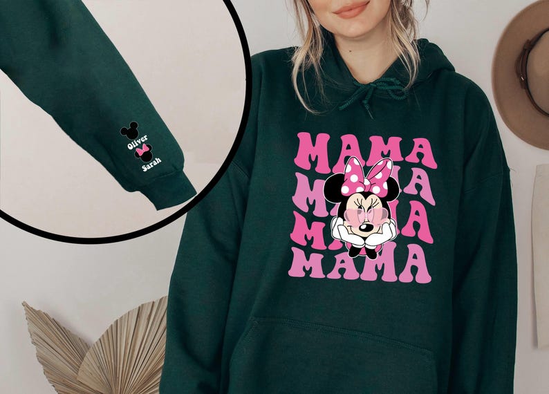 Puede incluir: Una sudadera con capucha verde oscuro con un gr&aacute;fico rosa y blanco de Minnie Mouse y la palabra "MAMA" repetida. La sudadera tiene una capucha con cord&oacute;n y un bolsillo canguro.