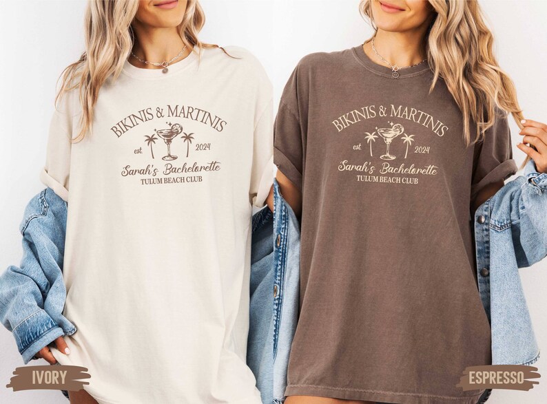 May include: Two oversized t-shirts with a graphic design featuring palm trees, a martini glass, and the text "Bikinis & Martinis est 2024 Sarah's Bachelorette Tulum Beach Club". The t-shirts are in ivory and espresso colors.