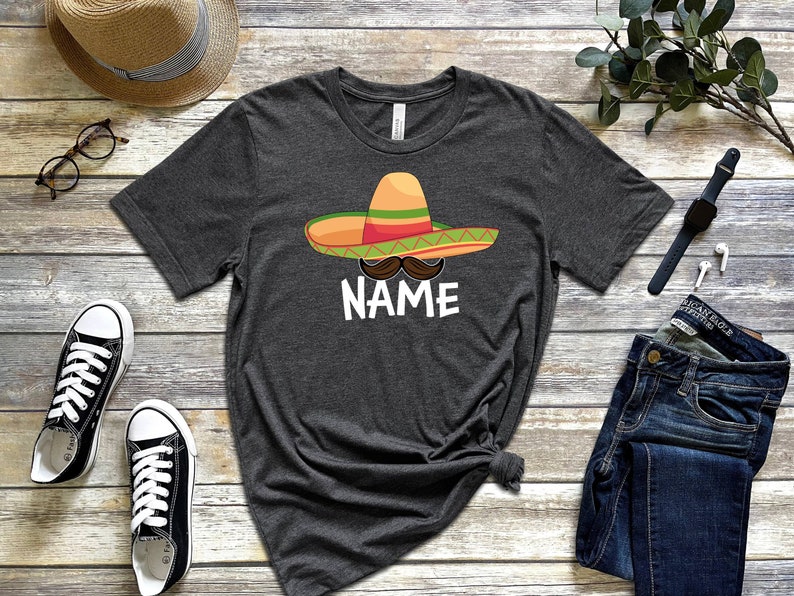 K&ouml;nnte beinhalten: Ein dunkelgraues T-Shirt mit einem Cartoon-Bild eines Sombreros, eines Schnurrbartes und dem Wort "NAME".