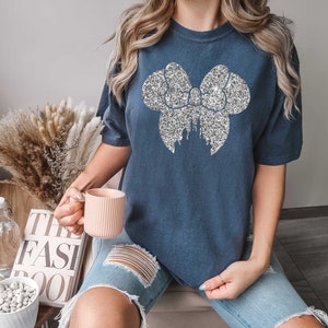 May include: A navy blue t-shirt with a silver glitter bow and castle design. The bow is large and covers most of the front of the shirt.