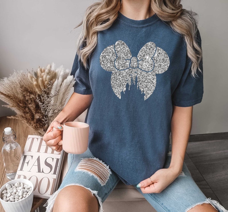 May include: A navy blue t-shirt with a silver glitter bow and castle design. The bow is large and covers most of the front of the shirt.