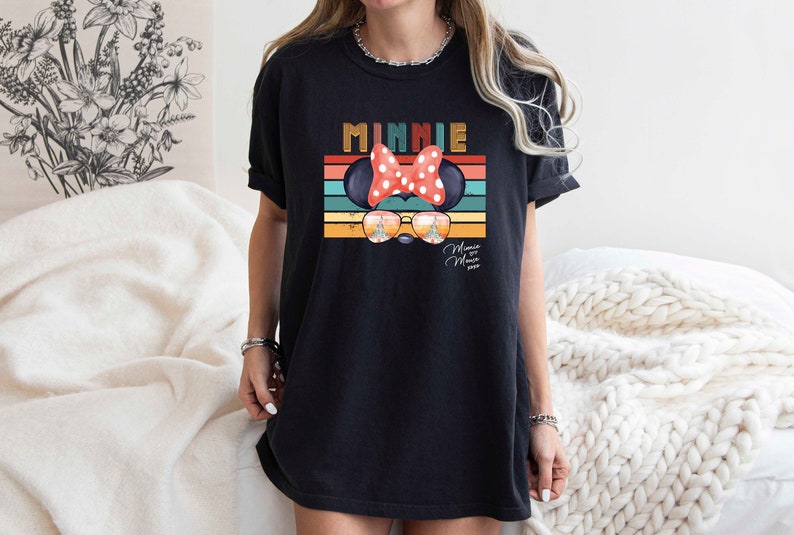Op de afbeelding: Zwart T-shirt met een retro-stijl grafische afbeelding van Minnie Mouse met een zonnebril en een rode strik. De afbeelding bevat de tekst "Minnie" en "Mouse House" in een vintage lettertype.