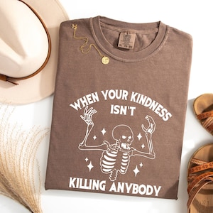 May include: A brown t-shirt with a white skeleton graphic and the text "When your kindness isn't killing anybody".