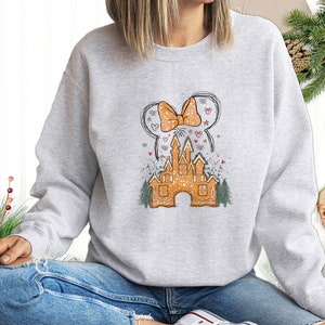 Puede incluir: Una sudadera gris con un castillo de jengibre y un lazo. El castillo est&aacute; decorado con chispas blancas y el lazo es rojo y blanco.