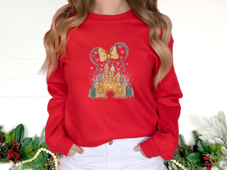 Puede incluir: Sudadera roja de manga larga con un gr&aacute;fico de un castillo de jengibre y un lazo, con un fondo nevado.