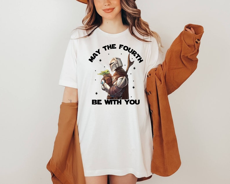 May include: White t-shirt with a black graphic of a Mandalorian character holding a baby Yoda with the text "May the Fourth Be With You".