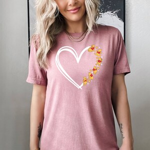 May include: A pink t-shirt with a white outline of a heart and Winnie the Pooh characters inside the heart.