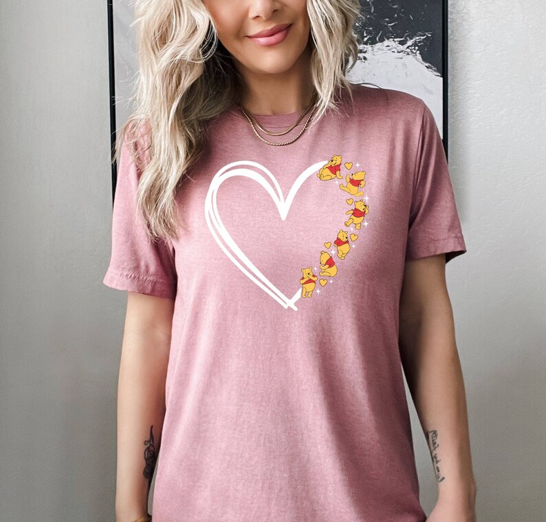 May include: A pink t-shirt with a white outline of a heart and Winnie the Pooh characters inside the heart.