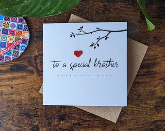 May include: A white card with black text that reads "to a special brother" and "happy birthday". A red heart button is hanging from a black branch drawn on the card.