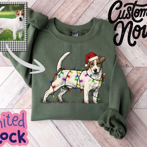 May include: Green sweatshirt featuring a Jack Russell Terrier wearing a Santa hat and Christmas lights. The sweatshirt has a photo of a Jack Russell Terrier on the upper left. Text on the image says "Customize Now" and "Limited Stock".