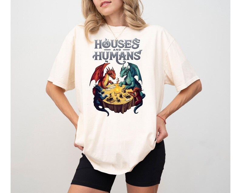May include: A white t-shirt with a graphic of three dragons playing a game around a table. The text "Houses and Humans" is above the dragons.