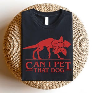 May include: Black t-shirt with a red graphic of a creature and the text "CAN I PET THAT DOG". The shirt is made of a soft material and is suitable for casual wear.