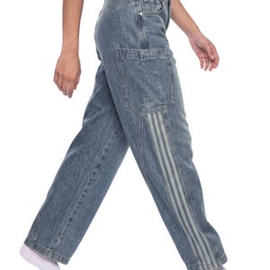May include: Mid-wash blue denim jeans featuring a high-waisted fit, a button and zipper fly closure, and large patch pockets on the thighs. The legs are detailed with vertical light-colored triple-stripe panels running down the outer sides.