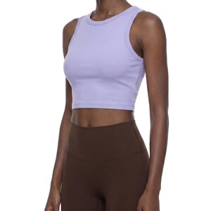 May include: A light purple sleeveless crop top with a crew neckline and ribbed trim around the armholes and neck. The top is paired with high-waisted dark brown leggings that feature a wide waistband and a smooth, fitted silhouette.
