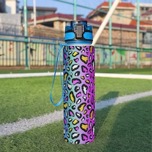 May include: A cylindrical water bottle featuring a vibrant gradient background transitioning from blue to purple, covered in a multi-colored leopard print pattern. The bottle includes a blue carrying strap and a dark blue locking lid mechanism.
