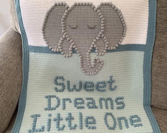 May include: A crocheted baby blanket featuring a gray elephant design on a white and light blue background. The blanket has a blue border and the words "Sweet Dreams Little One" are stitched in blue.