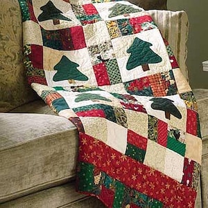 May include: A festive patchwork quilt with a Christmas tree design. The quilt features green tree appliqués on a white background, with red, green, and beige squares. The quilt is draped over a sofa, showcasing its festive design.
