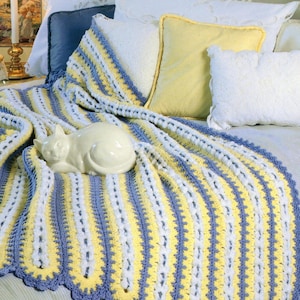 Può includere: Una coperta all'uncinetto fatta a mano in giallo, bianco e blu, con un bordo smerlato, drappeggiata su un letto. Una statuina di gatto in ceramica bianca poggia sulla coperta, circondata da cuscini bianchi e gialli. Dimensioni: circa 180 cm x 200 cm.
