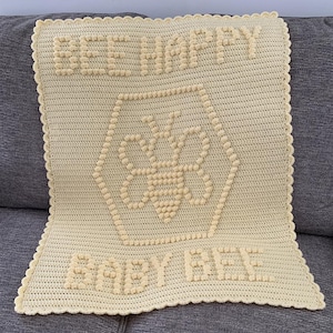 May include: A yellow crocheted baby blanket with a bee design and the text "Bee Happy Baby Bee".
