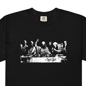 May include: Black t-shirt with a white graphic of a group of people sitting at a table, with the text "The Last Set" below the image.