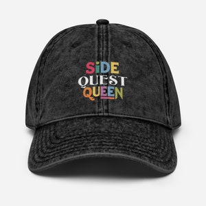 Könnte beinhalten: Schwarze Baseballkappe aus Denim mit einem bunten gestickten Design, das "Side Quest Queen" lautet.