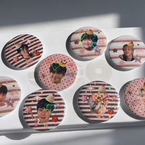 Op de afbeelding: Een verzameling van acht ronde pins. De pins bevatten afbeeldingen van mensen met decoratieve elementen zoals cupcakes, harten en sterren. De achtergronden zijn roze en wit gestreept of gestippeld.